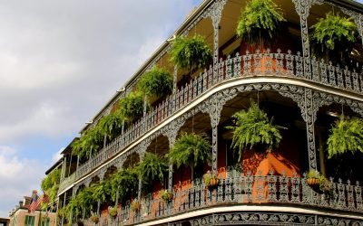Detailed view of ornate ironwork balconies with lush greenery in New Orleans under a vibrant sky.